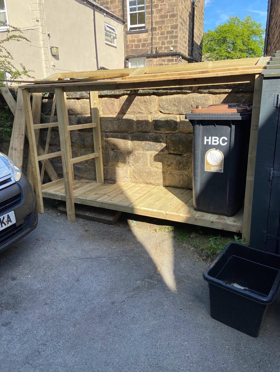 Custom-built timber bin store against a stone wall.