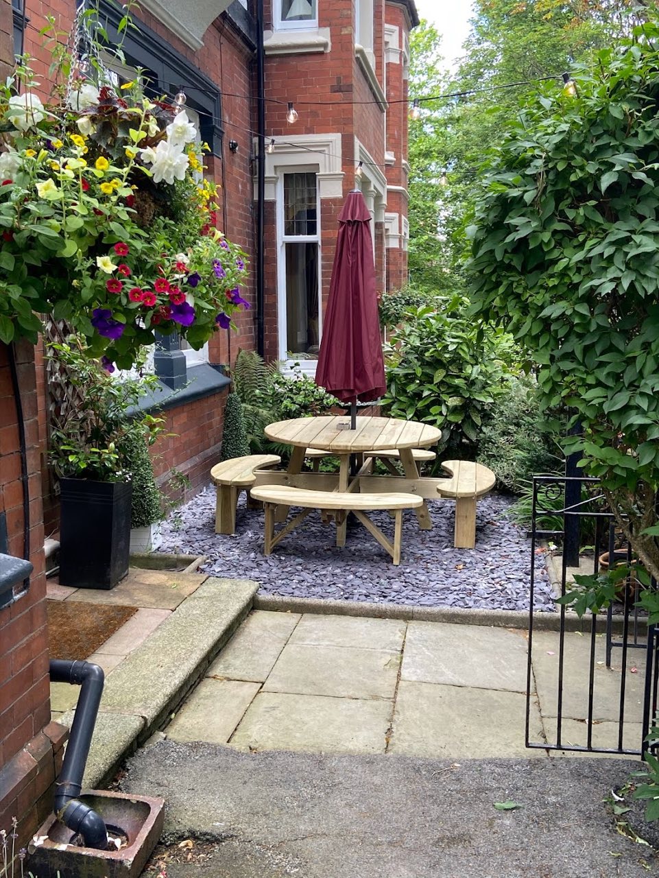 Tidy front courtyard garden with a bench, hanging baskets and clean paving.