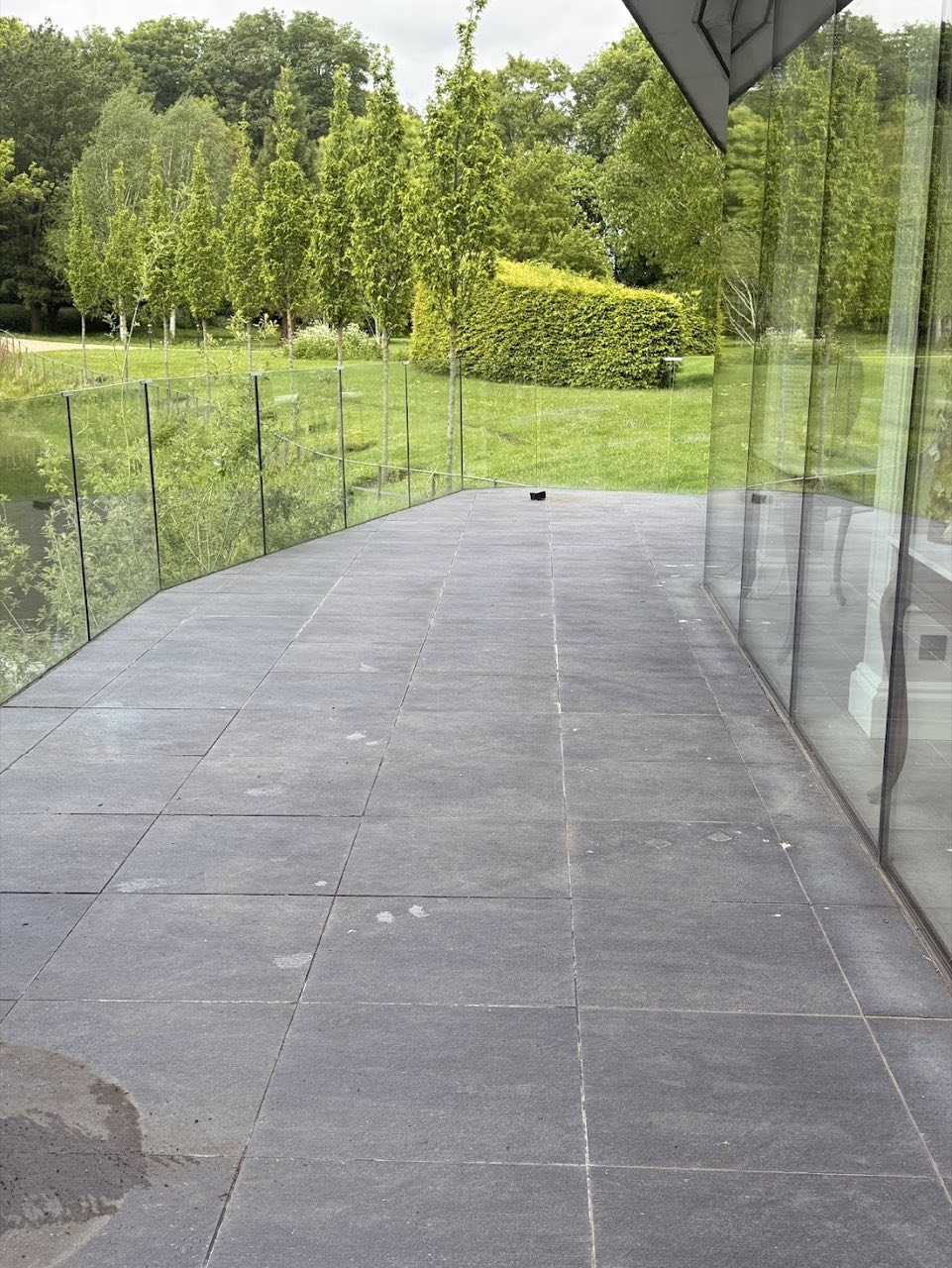 Dark stone patio before jet washing, beside a glass garden room.